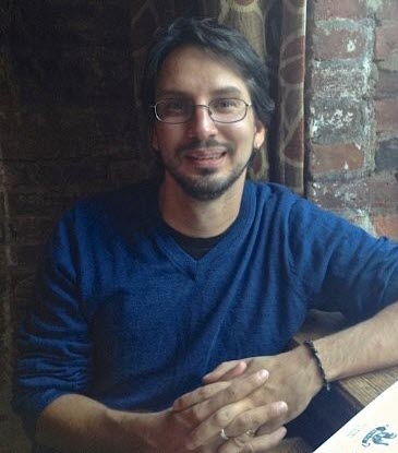 Man with dark hair, wearing a dark blue three-quarter length sleeved shirt and glasses