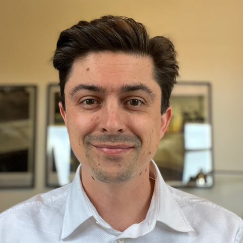 Smiling man with dark hair wearing a white collared shirt