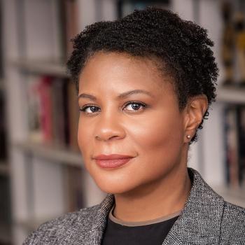 Portrait of an African American woman with short dark hair, wearing a grey tweed blazer and black shirt.