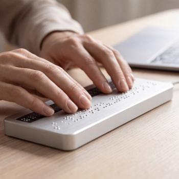Person's hands reading a braille display connected to a laptop